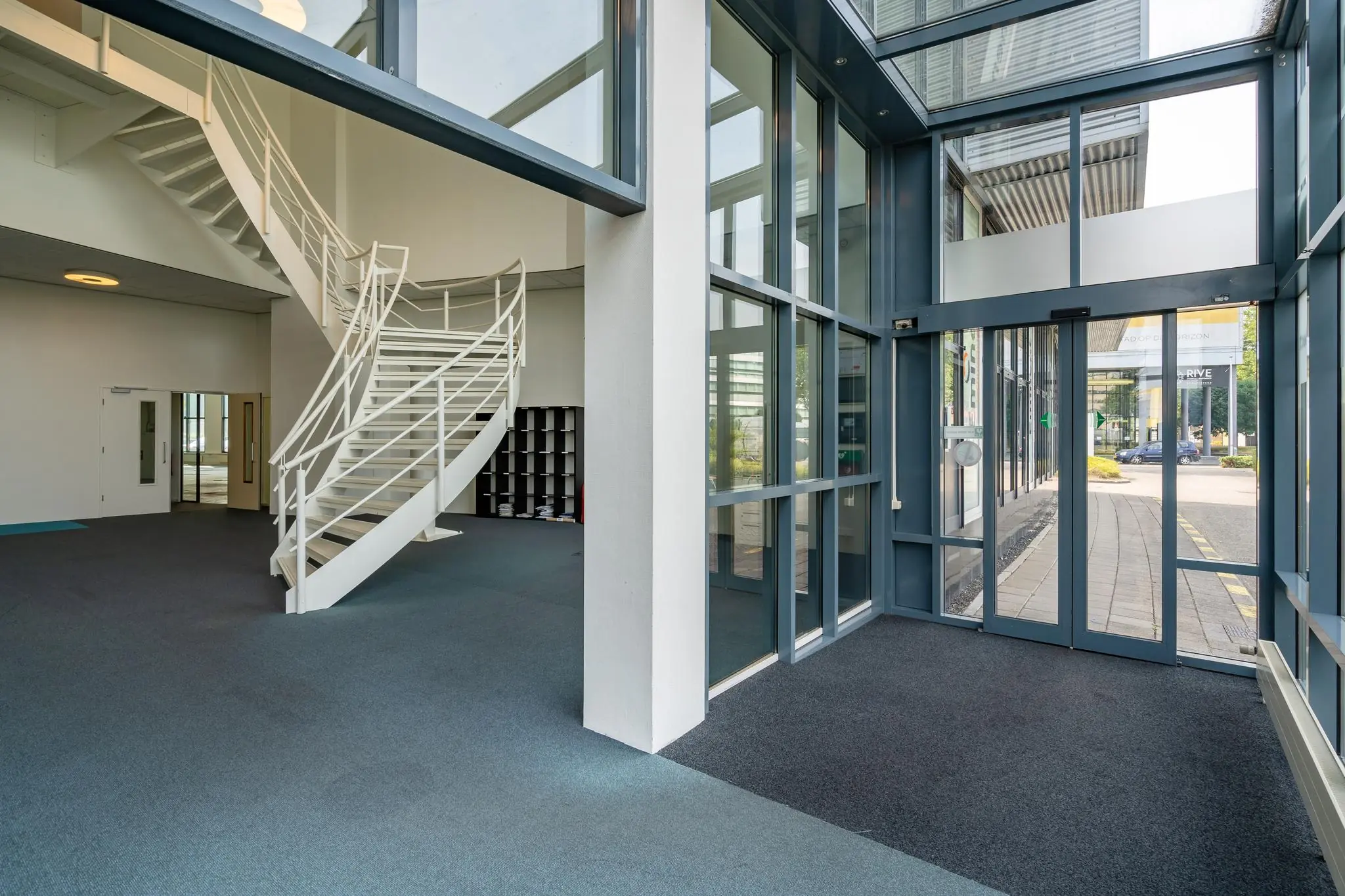 Moderne entreehal van een kantoorgebouw aan de Rivium Boulevard met glazen gevel en witte spiltrap.